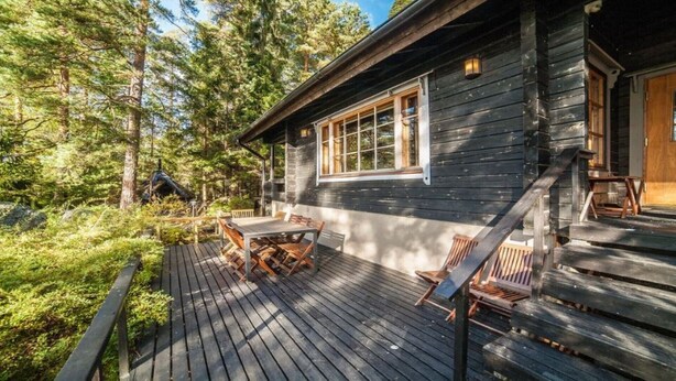 A wooden cabin with a deck, a table, and chairs. - Skitunäs Seaside villa in Pyhtää (Pyhtää)