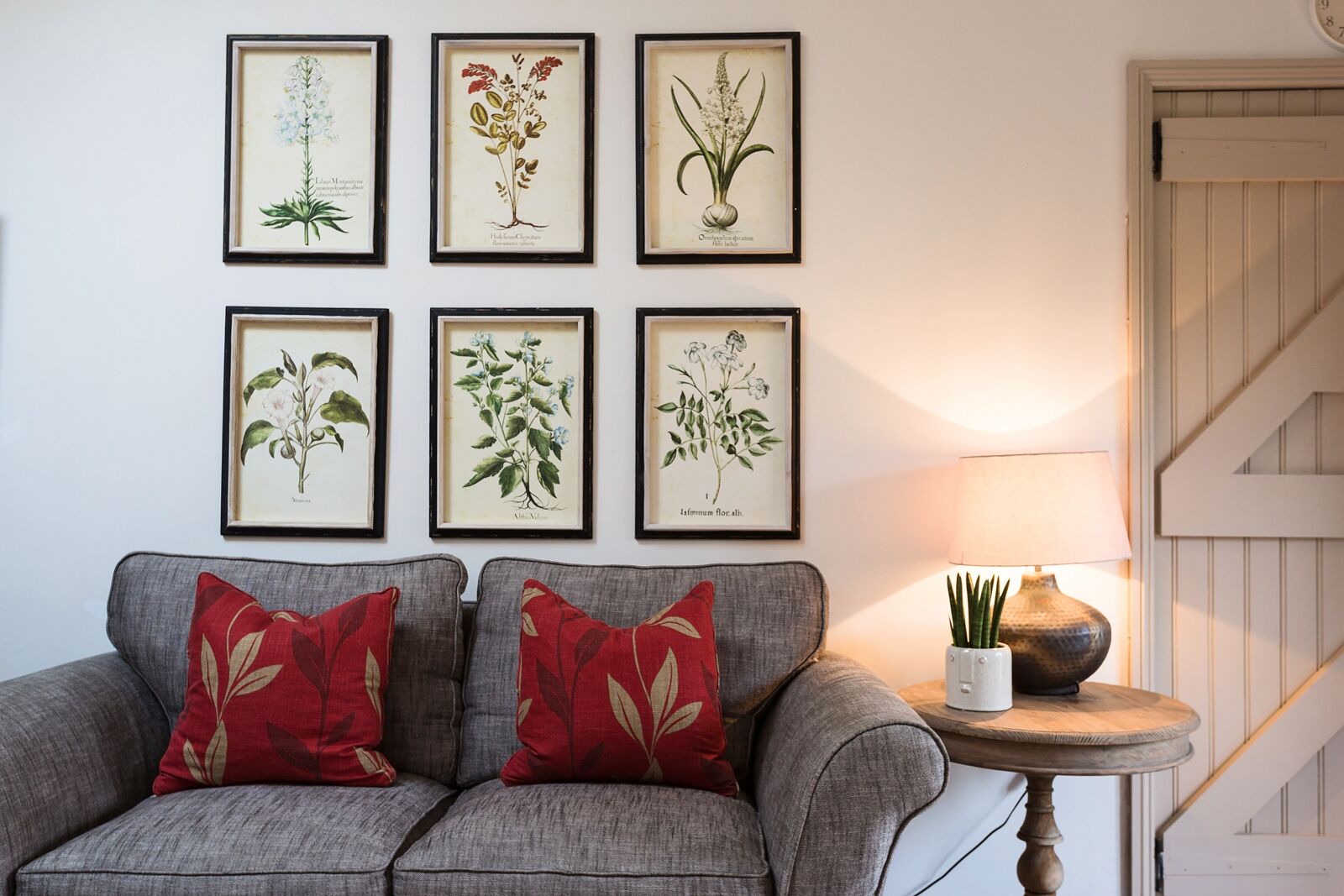 A living room with a grey sofa, red patterned cushions, and a small table with a lamp.