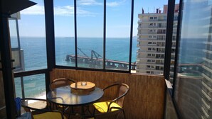 A balcony with a view of the sea, a table, and wicker chairs.
