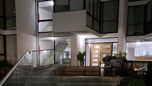 A staircase leading to a building entrance with a metal railing, a potted plant, and a bench.