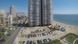 A high-rise building with multiple balconies, a parking lot, and a beach in the background.
