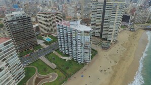 A high-rise building with multiple balconies, a swimming pool, and a beach area with people.