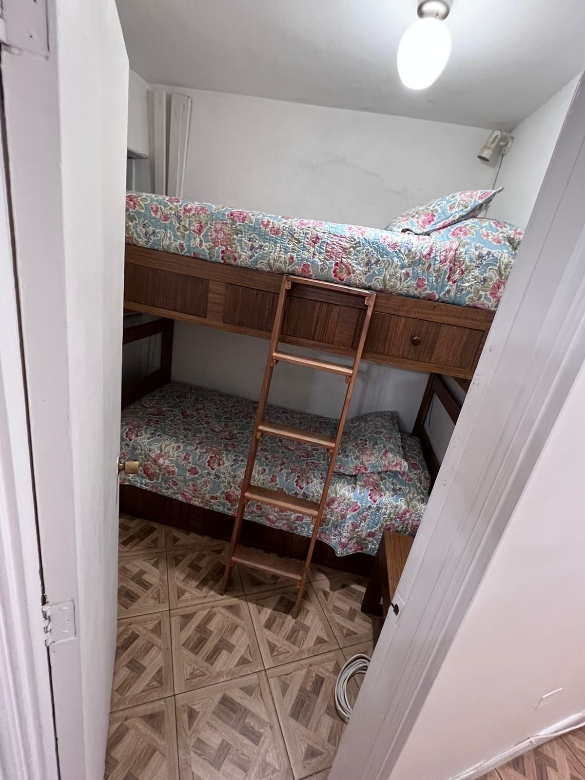 Un lit superposé avec une literie à motifs floraux, une échelle en bois et un sol carrelé.