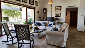 A spacious living room with a sofa set, a rocking chair, and a coffee table. There are framed pictures on the wall and a clock. - Beautiful villa in the middle of nature, 5 minutes away from the best beaches of Mallorca. (Muro)
