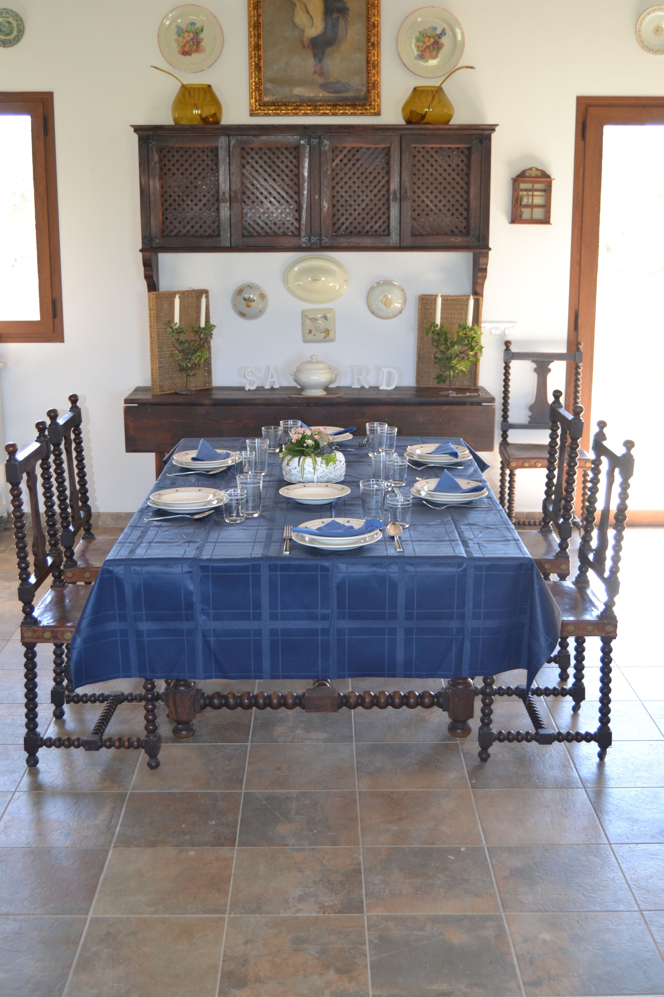 A dining table set with plates, glasses, and cutlery, flanked by chairs with ornate wooden legs.
