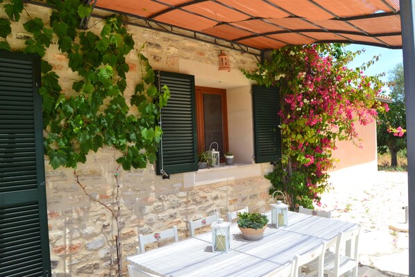 A stone building with green shutters, a table with chairs, and potted plants. - Beautiful villa in the middle of nature, 5 minutes away from the best beaches of Mallorca. (Muro)