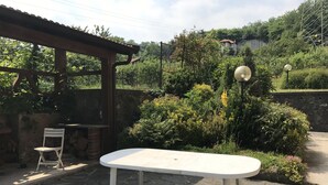 A patio with a white table and chairs, surrounded by stone flooring and lush greenery. - Just 4 km from Arona, in Meina Villa, surrounded by greenery with views of Lake Maggiore and Rocca Angela. (Pisano)