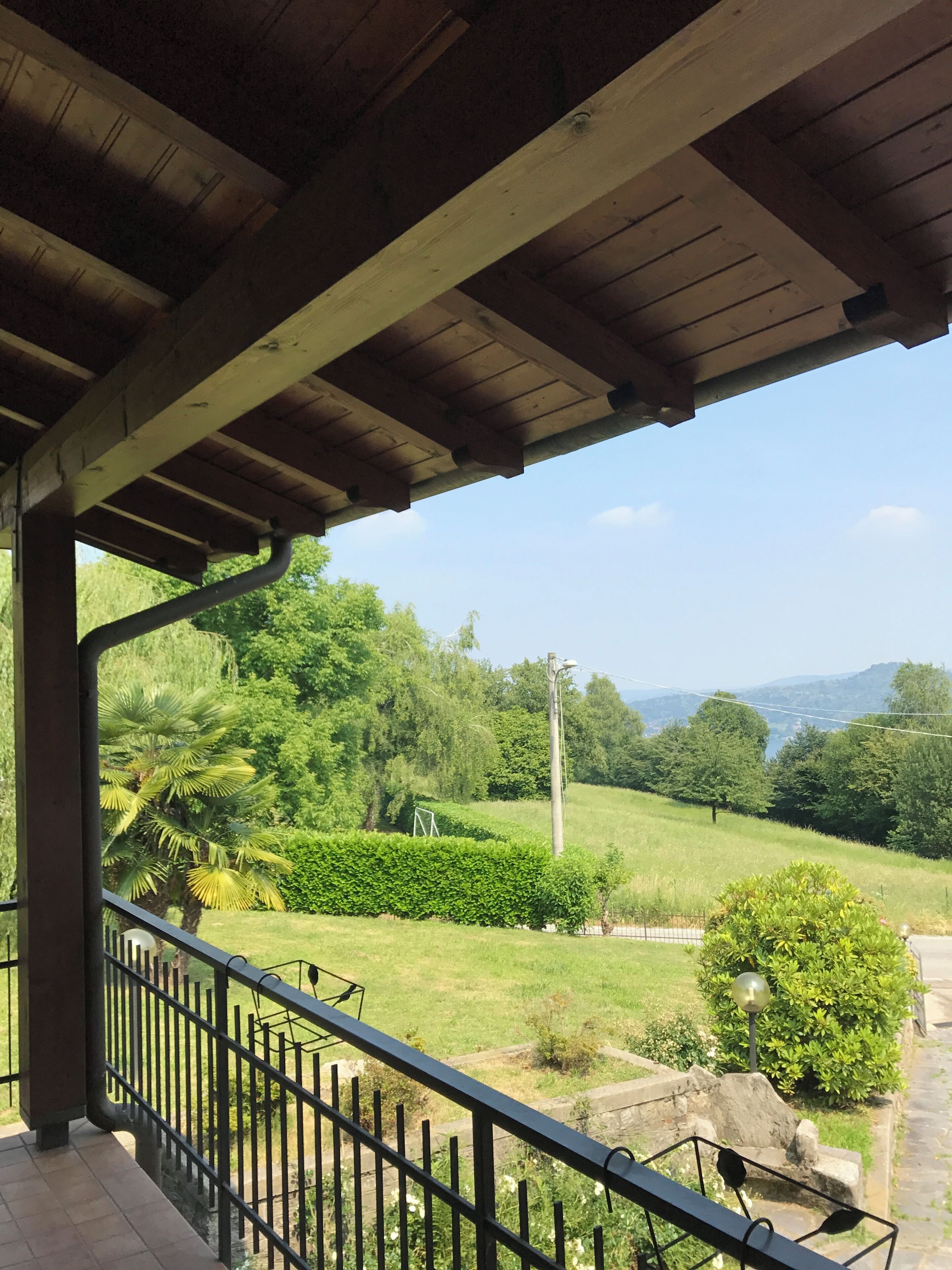Un espacio al aire libre techado con vista a un paisaje verde, que incluye árboles y un cielo despejado.