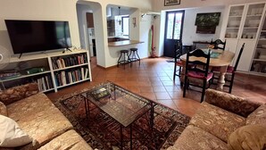 Een woonkamer met een televisie, boekenplanken, een salontafel en een eethoek met stoelen en een tafel.