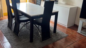 Et spiseområde med et bord og stole, udsigt gennem en glasdør, og et hvidt skab med et fladskærms-TV.