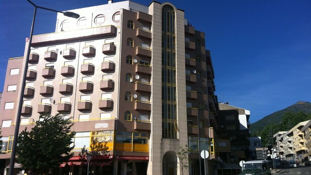 Et hotel med flere etager, et centralt vertikalt glastårn, flere balkoner og en restaurant i stueplan.
