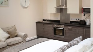 A modern bedroom with a skylight, a bed with white bedding, a bedside table, a built-in oven, and a microwave. - Toothbrush Apartments - Central Ipswich East - Rope Walk (Ipswich)