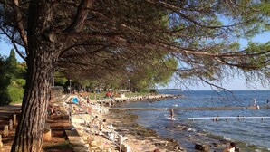 Une plage avec une promenade bordée de pierres, des gens qui prennent des bains de soleil et une vue sur la mer.