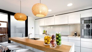 Una cocina moderna con encimera de madera, taburetes de bar blancos y dos lámparas colgantes.