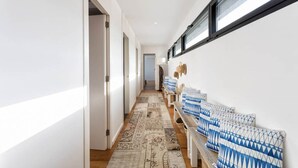 Un pasillo con un rug adornado, un banco con cojines azul y blanco, y una estantería con objetos decorativos.