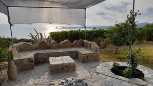 An outdoor seating area with stone benches and a fire pit, overlooking a body of water and hills.