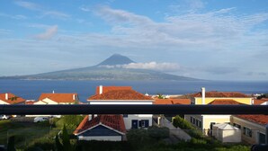 A coastal view with a mountain in the background, houses with red-tiled roofs, and a clear sky.