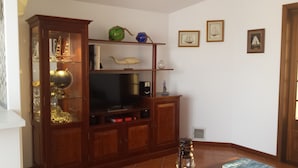 A living room with a wooden cabinet containing a television, decorative items, and a globe. There are framed pictures on the wall and a door to the right.