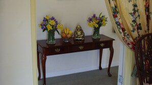 A wooden console table with floral vases and fruit bowl against a white wall, under a framed floral artwork.