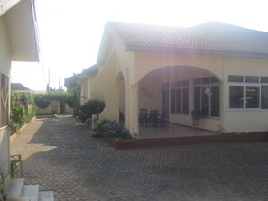 A building with a tiled roof, a covered patio area with chairs, and a paved courtyard. - Three bedroom self- catering apartment with  pool- fully self contained  V3 (Accra)