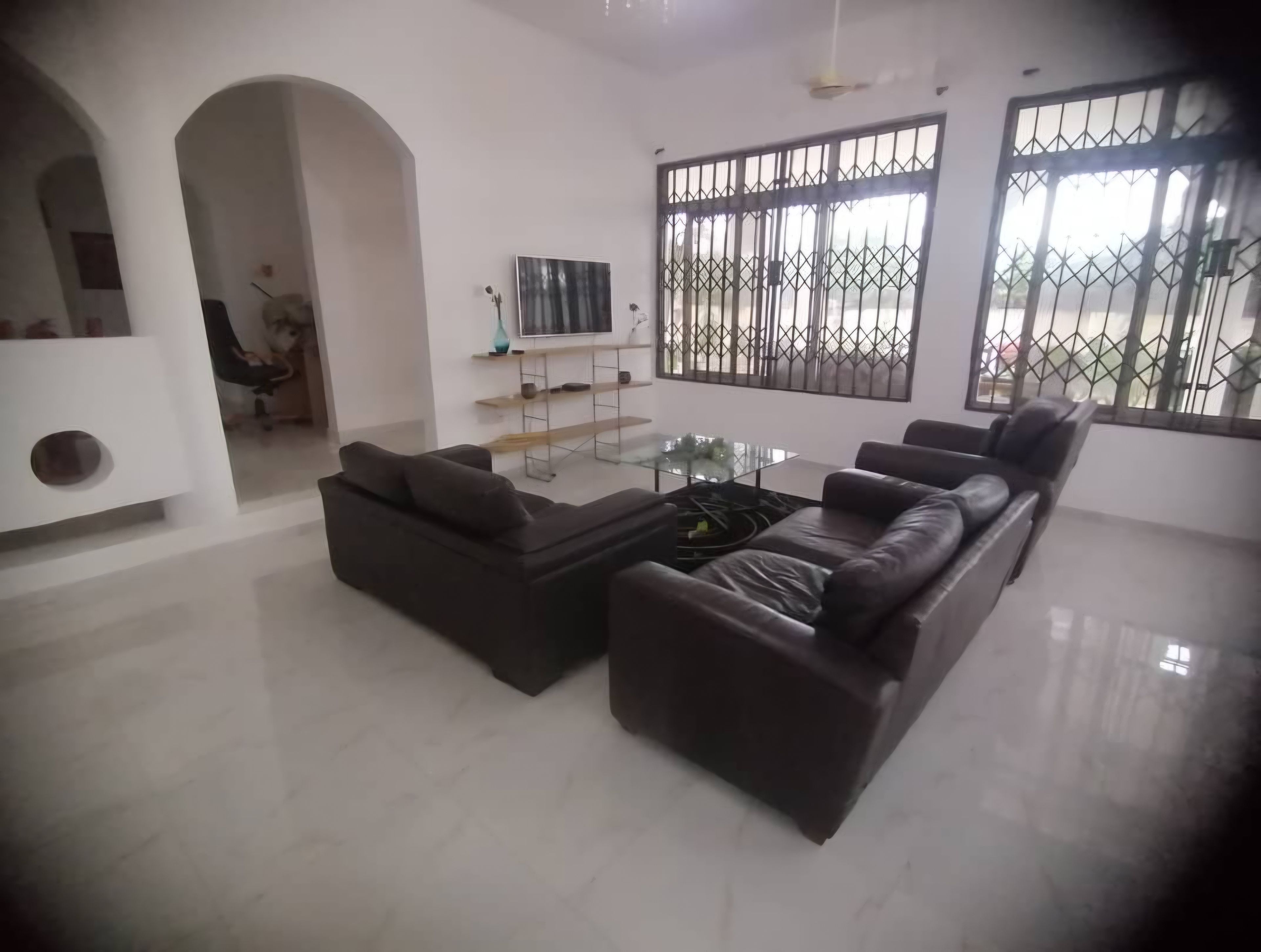 A modern living room with a sectional sofa, a glass coffee table, and a TV mounted on the wall.