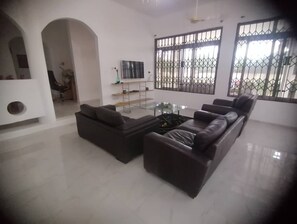 A modern living room with a sectional sofa, a glass coffee table, and a TV mounted on the wall.