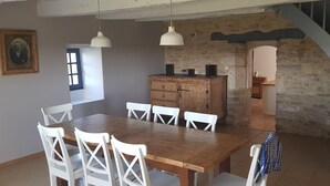 A dining area with a wooden table and white chairs, a wooden cabinet, and a stone wall. - Le Petit Paradis - Cottage for 8 people with Private Pool in the Countryside (Caylus)