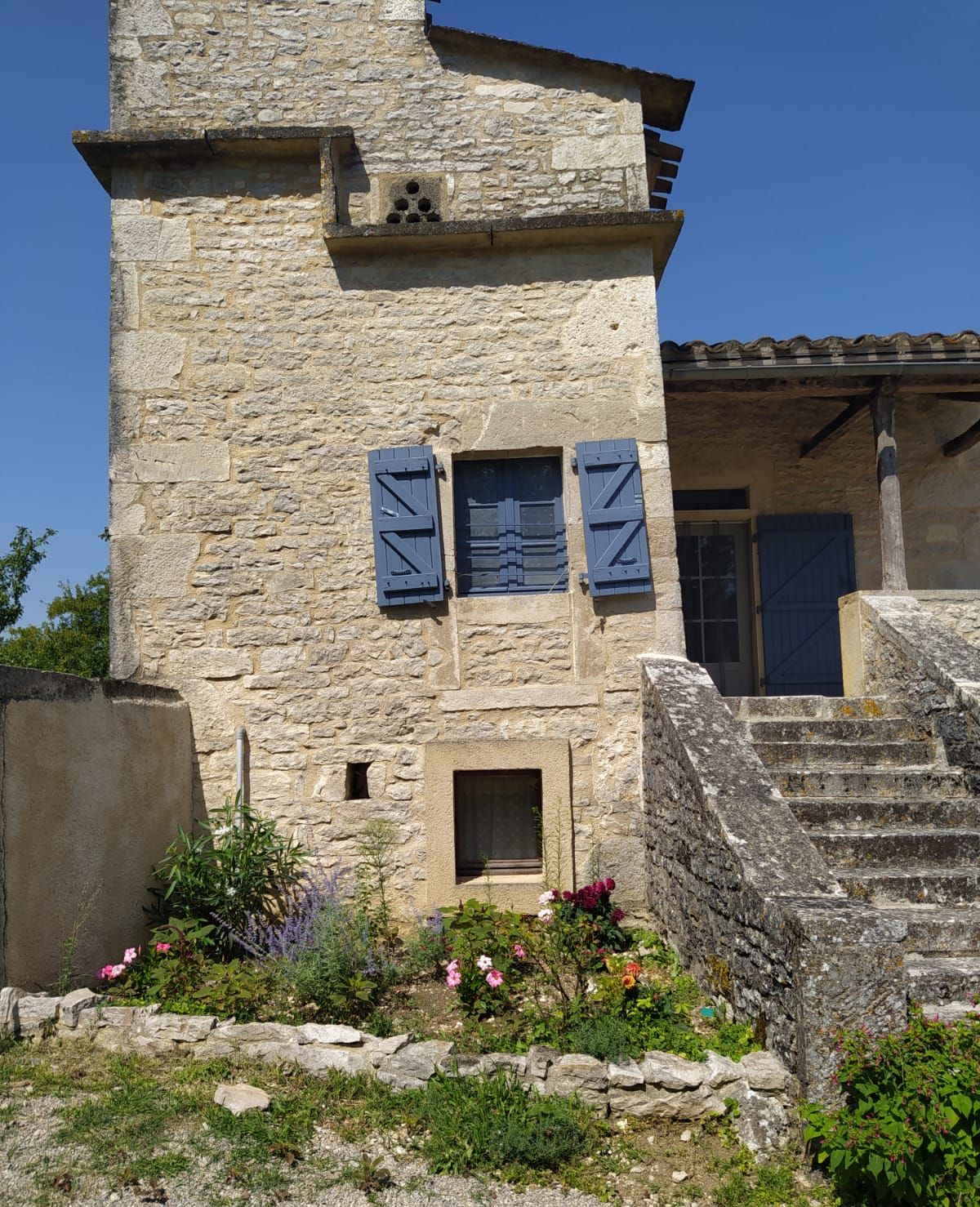A stone building with a tower, a small window with shutters, and a staircase leading to a door.