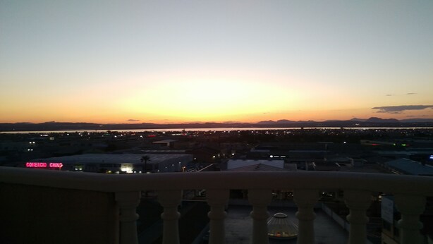 Une vue sur le coucher de soleil depuis un balcon donnant sur une ville, avec une chaîne de montagnes visible au loin.