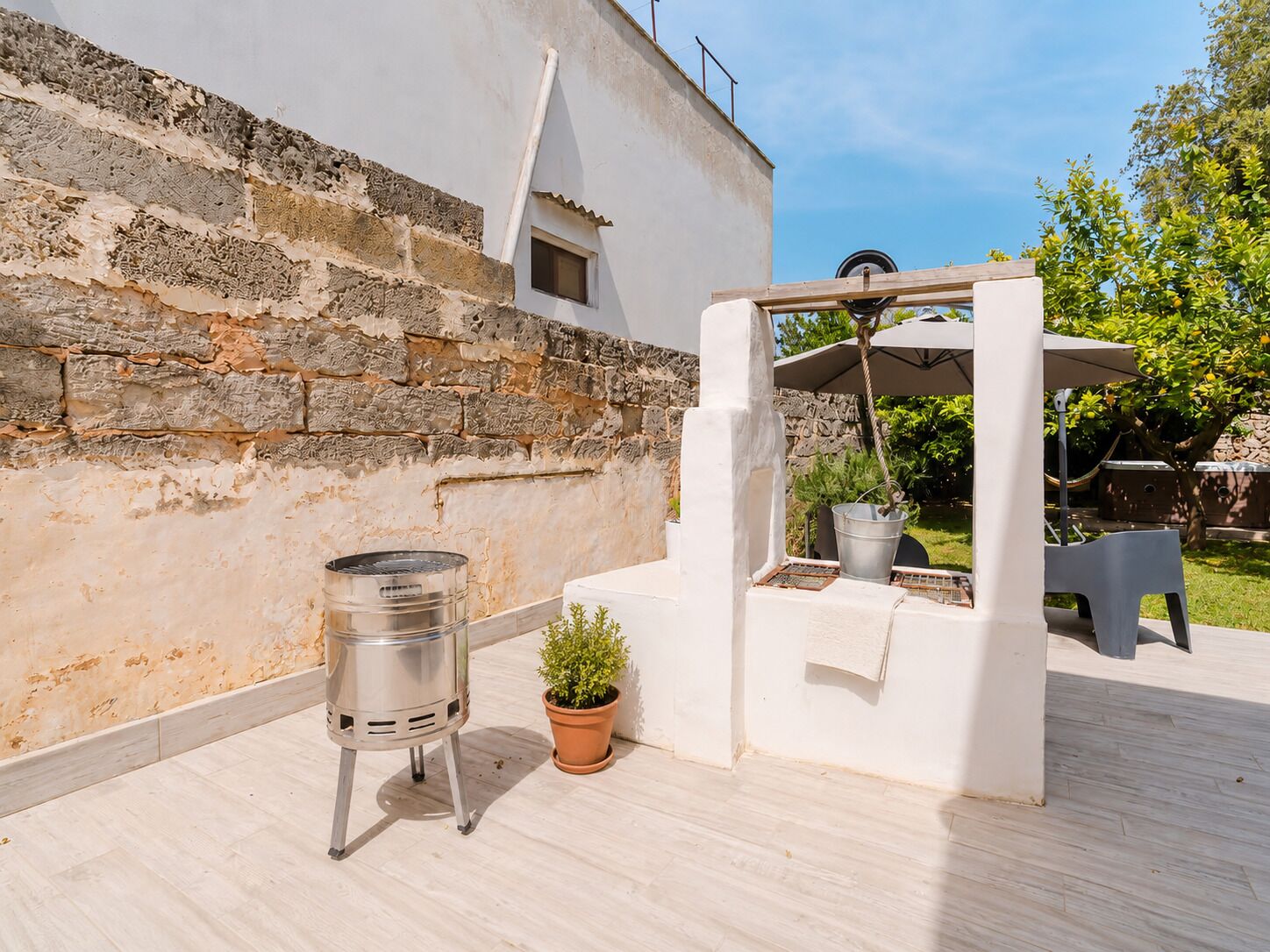 Un espace patio comprenant un barbecue, un pot de fleurs et un gazebo blanc avec une table et des chaises.