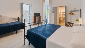 Ein Schlafzimmer mit zwei Betten, einem Fernseher, einem Schminktisch und Blick auf die Küche.