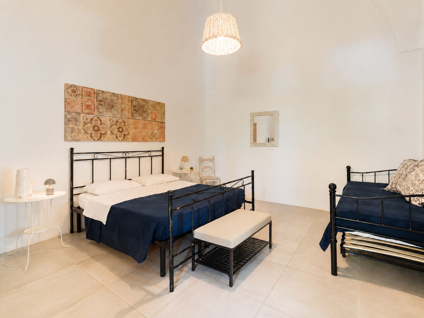 A bedroom with a bed, bench, bedside table, lamp, and a hanging light fixture.