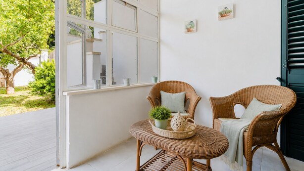 Ein Zimmer mit großem Fenster, Korbmöbeln und einem kleinen Tisch mit einer Pflanze.
