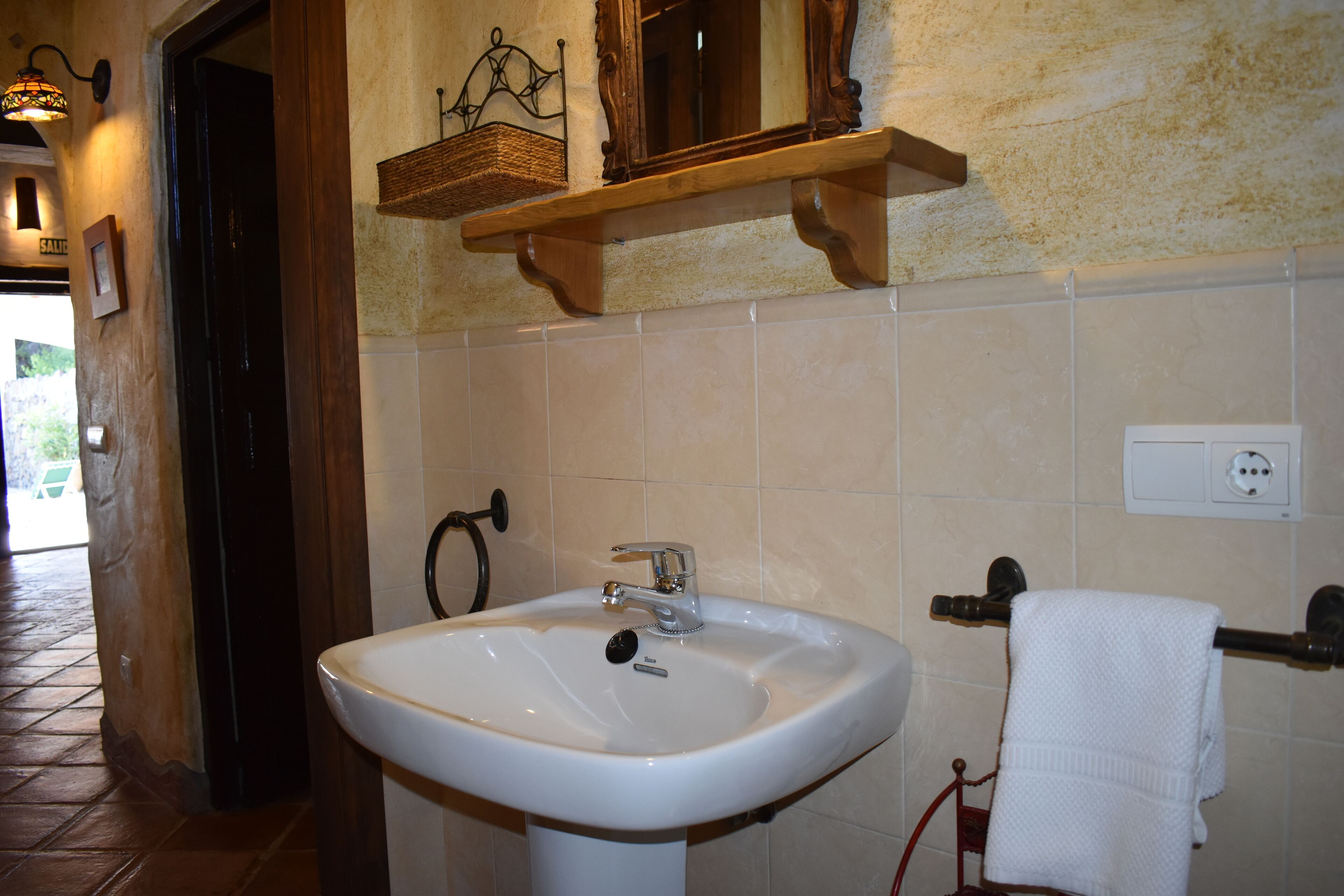 A bathroom with a white sink, a wooden shelf above it, and a towel rack to the right.