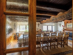 A dining area with wooden chairs and a table, a wooden ceiling, and a view through a frosted glass window. - The House of Pedros (Villar)