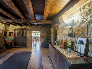A rustic interior with stone walls, wooden beams, a reception desk, and a view to a patio area. - The House of Pedros (Villar)