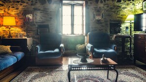 Una habitación acogedora con paredes de piedra, un ventanal grande, dos sillones, una mesita con un cuenco y un televisor sobre un mueble de madera.