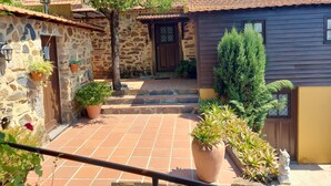 Un edificio de piedra con un patio empedrado, plantas en macetas y una estructura de madera.