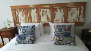 Una cama con dos almohadones estampados, un cabecero de madera y una mesita de noche con lámpara y botella.