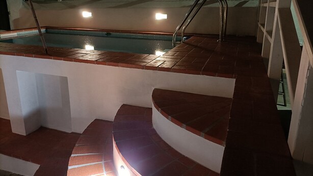 Una piscina con escalones que bajan al agua, rodeada por un muro blanco y una valla de metal.