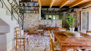 A rustic interior with a stone floor, wooden furniture, a bookshelf, and a dining area.