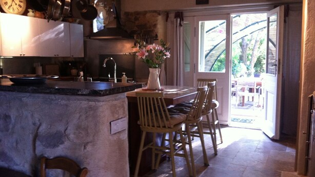 A kitchen with a stone island, wooden chairs, and a view of the outdoors through a glass door.