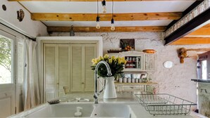 A kitchen with a white sink, wooden beams, a hanging light fixture, and a vase of yellow flowers.
