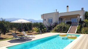 Una piscina con dos flotadores, una silla de descanso y una sombrilla.