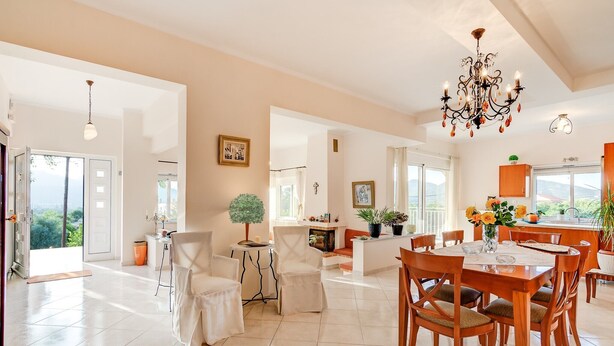 Un comedor amplio con una mesa y sillas de madera, una araña y vistas al exterior.