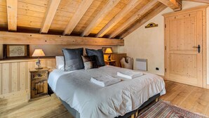 Een slaapkamer met een houten plafond, een bed met kussens, een nachtkastje, een lamp en een kledingkast.