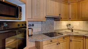 Een keuken met houten kasten, een Bosch magnetron, een roestvrijstalen waterkoker, granieten aanrechtbladen en een spoelbak met kraan.
