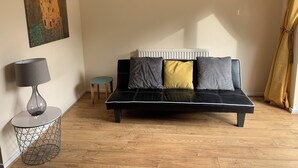 A living room with a black sofa, a small round table, a lamp, and a radiator. - Cosy Corner House. (Kettering)