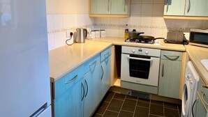 A compact kitchen with light blue cabinets, a white refrigerator, a stove, an oven, and a washing machine. - Cosy Corner House. (Kettering)