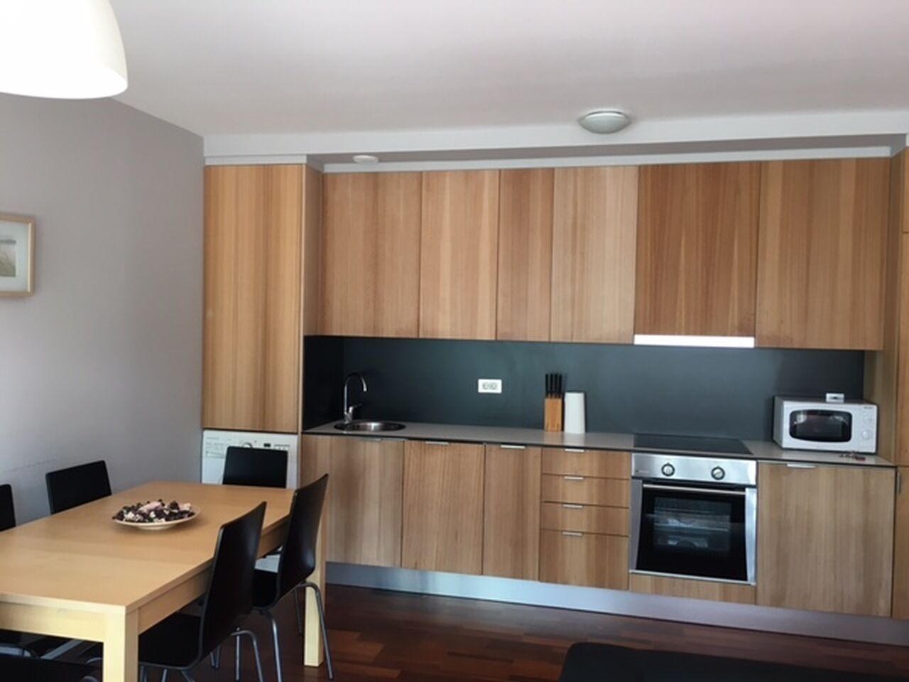 A modern kitchen with wooden cabinets, a stainless steel sink, a microwave, and an oven.